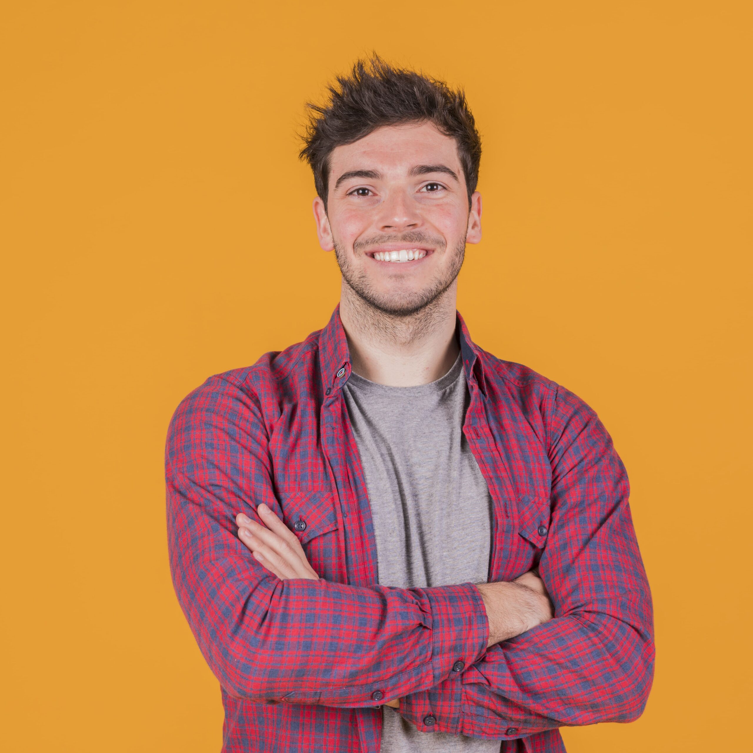 portrait-smiling-young-man-with-his-arm-crossed-standing-against-orange-backdrop